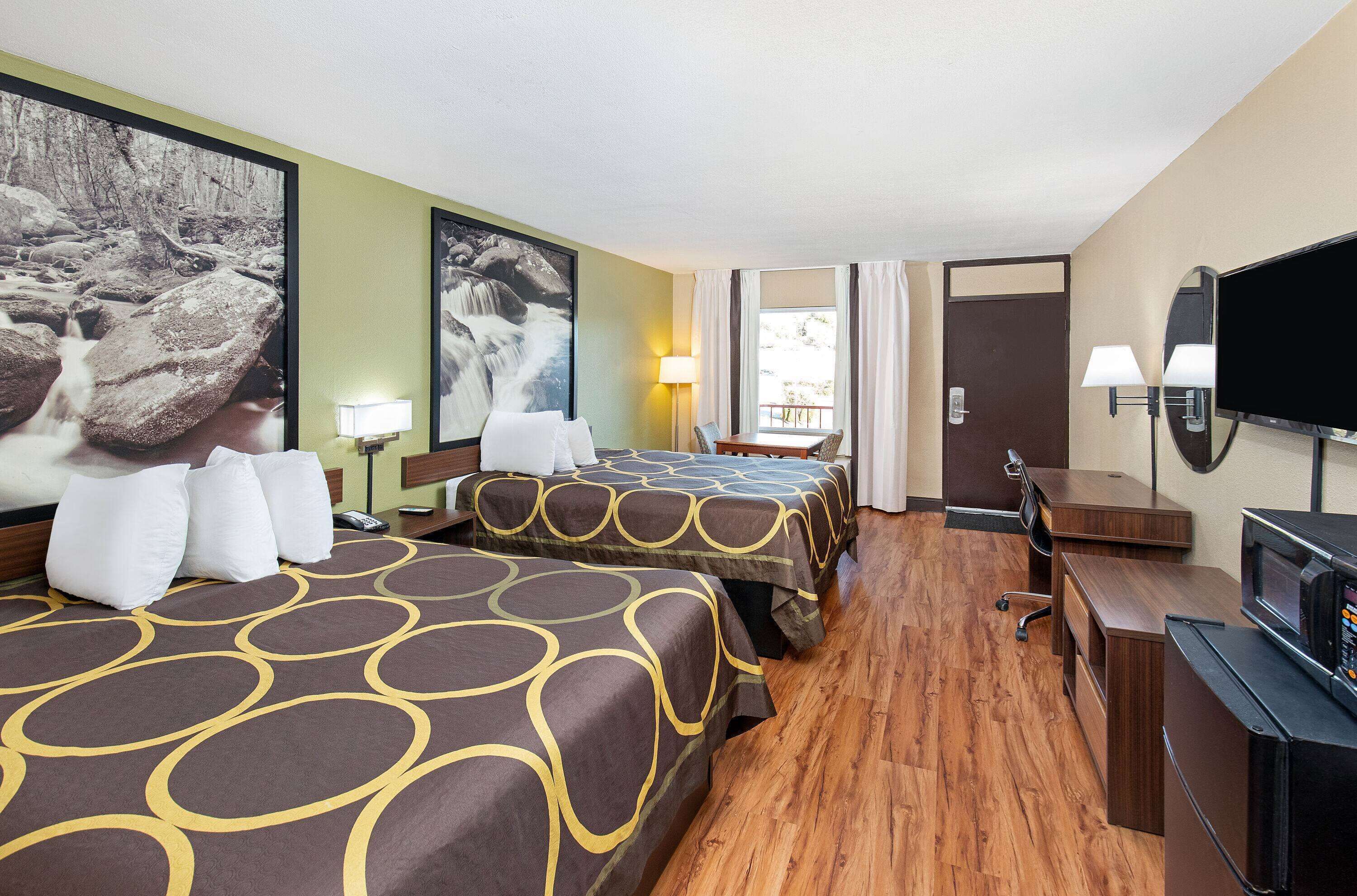 Une chambre d’hôtel avec deux lits, un bureau, une télévision et une fenêtre avec des rideaux.
