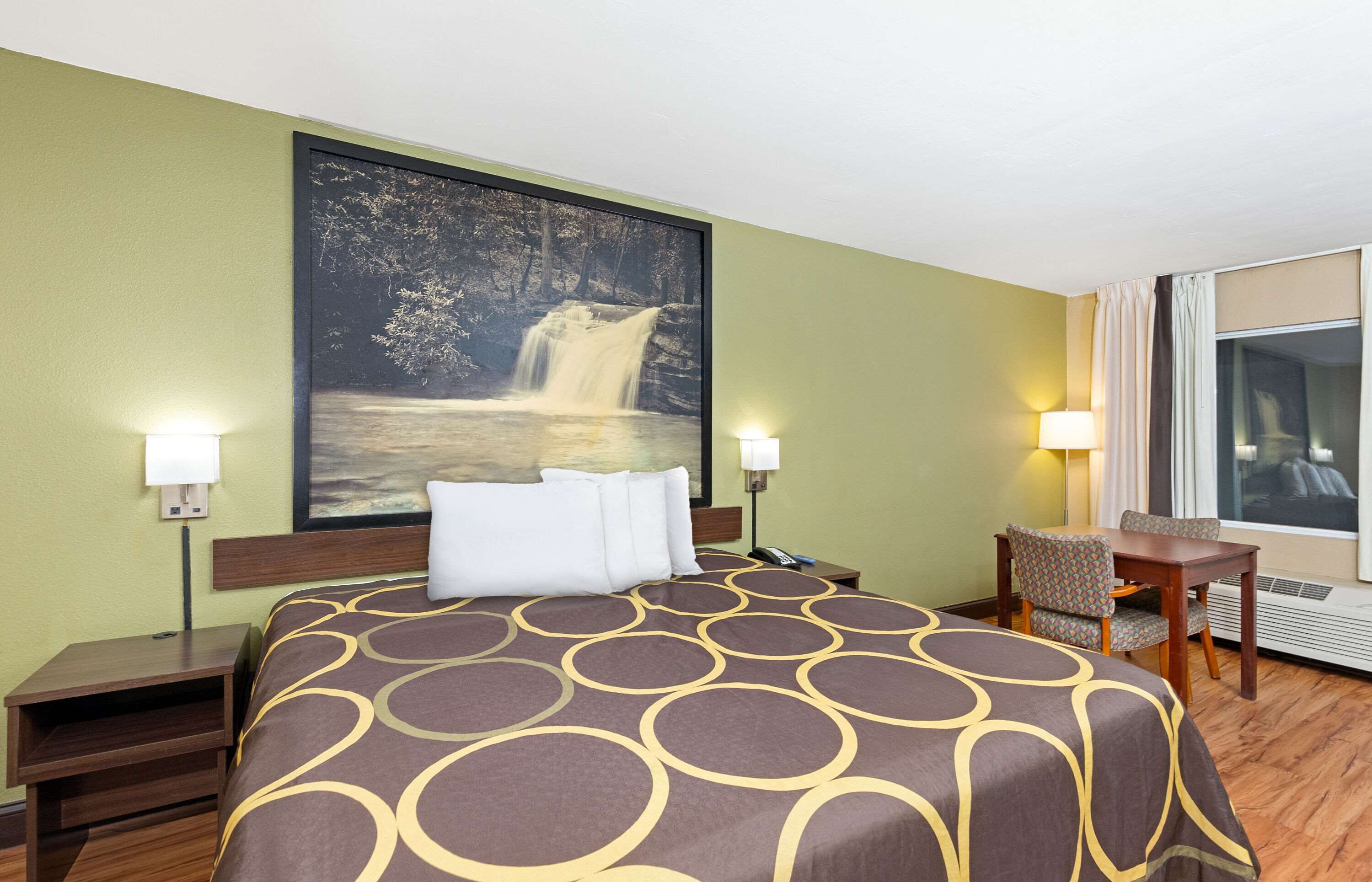 Quarto de hotel com uma cama grande, duas mesas de cabeceira, uma escrivaninha com cadeira e uma janela ampla.