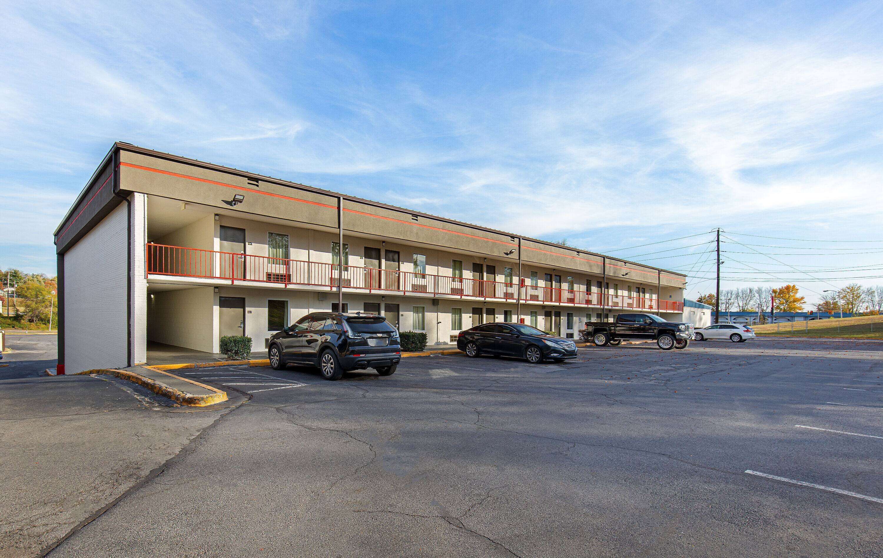 A motel with a two-story structure, a parking lot, and several vehicles parked in front.