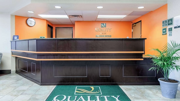 A reception desk with a clock, a sign for Quality Inn by Choice Hotels, and a green carpet with the hotel logo. - Quality Inn Junction City - Near Fort Riley (Junction City)