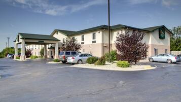 Un Quality Inn con estacionamiento techado, varios coches aparcados y cielo despejado.