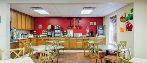 A dining area with wooden cabinets, a red wall, and a kitchen counter with various appliances and food items.