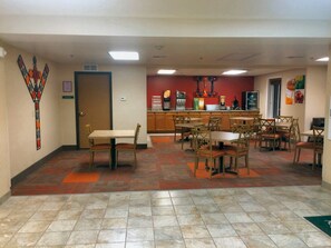 A dining area with multiple tables and chairs, a kitchen area with a coffee machine, and a door with a sign.