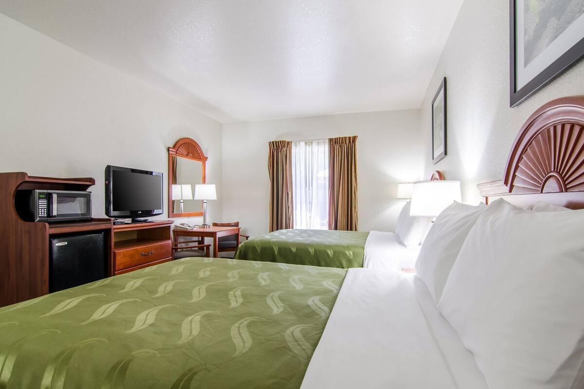 A hotel room with two beds, a desk with a computer, a television, a microwave, and a small refrigerator.
