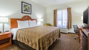 A hotel room with a bed, two bedside tables, a desk with a chair, a television, and a window with curtains. - Quality Inn Junction City - Near Fort Riley (Junction City)