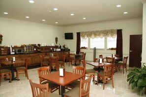 A dining area with wooden tables and chairs, a kitchen area with appliances, and a television mounted on the wall.
