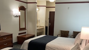 A hotel room with two beds, a dresser, a mirror, a vanity with a sink, and a door leading to another room.