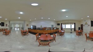A spacious dining area with multiple wooden tables and chairs, a central counter with a coffee station, and a large window providing natural light.