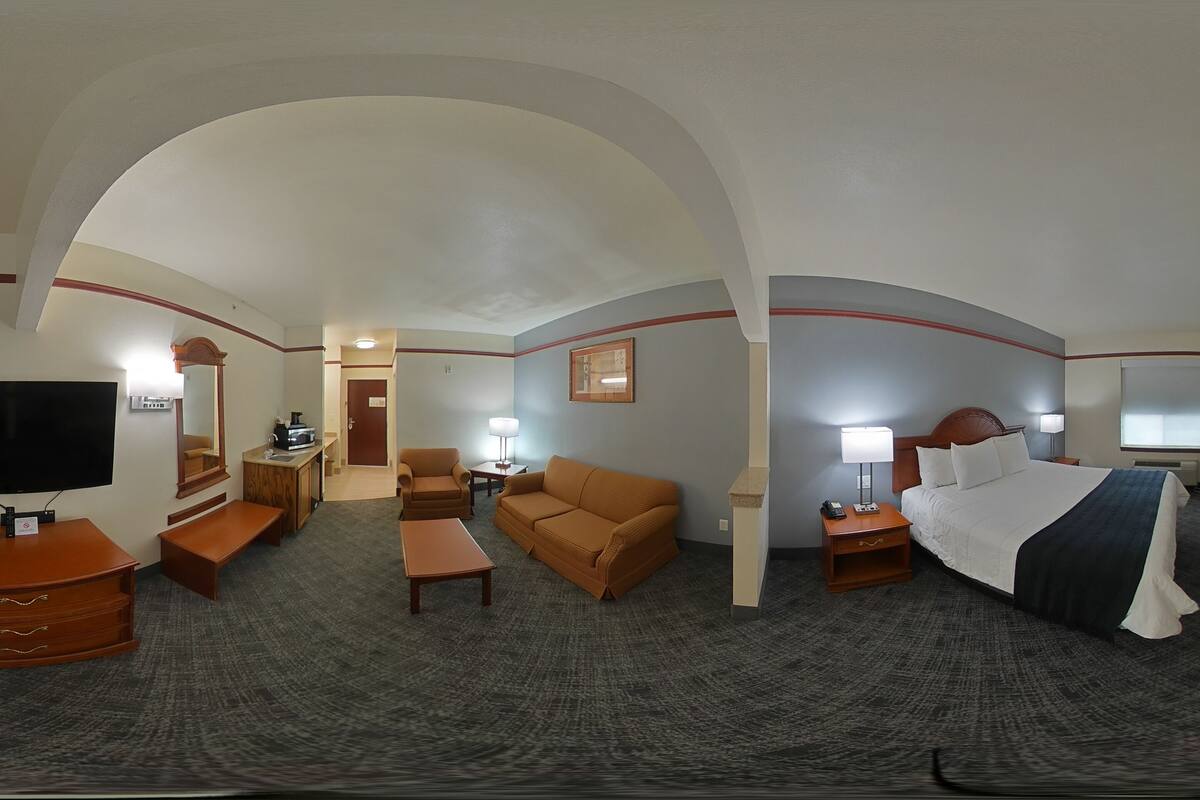 Quarto de hotel com cama, sofá, escrivaninha, televisão e banheiro.