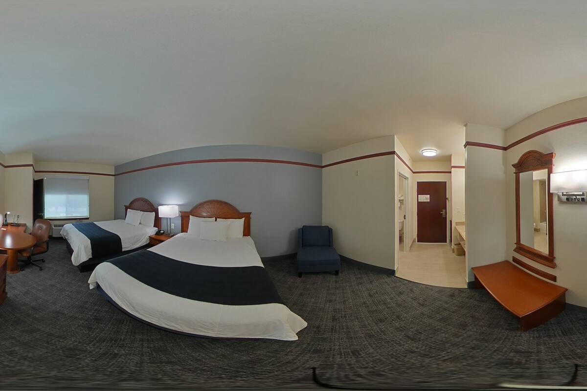 Quarto de hotel com duas camas, uma escrivaninha com televisão, uma cadeira e um banco.