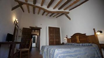 Quarto com teto de madeira, cama com colcha estampada, escrivaninha com cadeira e televisão.