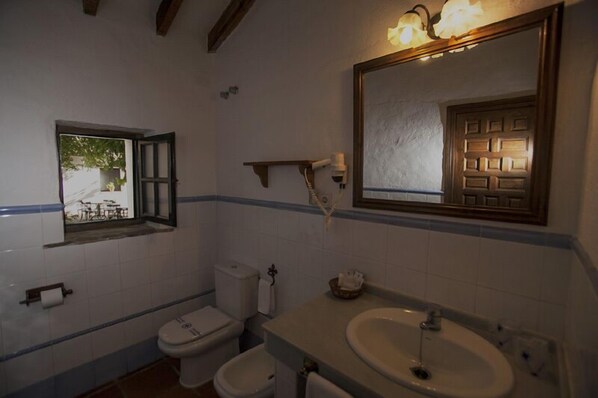 A bathroom with a toilet, bidet, sink, and a mirror with a light fixture. - Hotel El Horcajo (Montecorto)