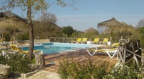 A pool area with lounge chairs and a thatched-roof structure.