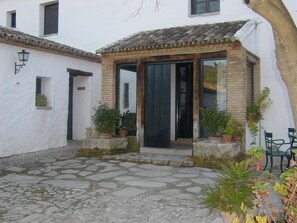 A courtyard with a stone floor, a small brick structure with a tiled roof, and potted plants.