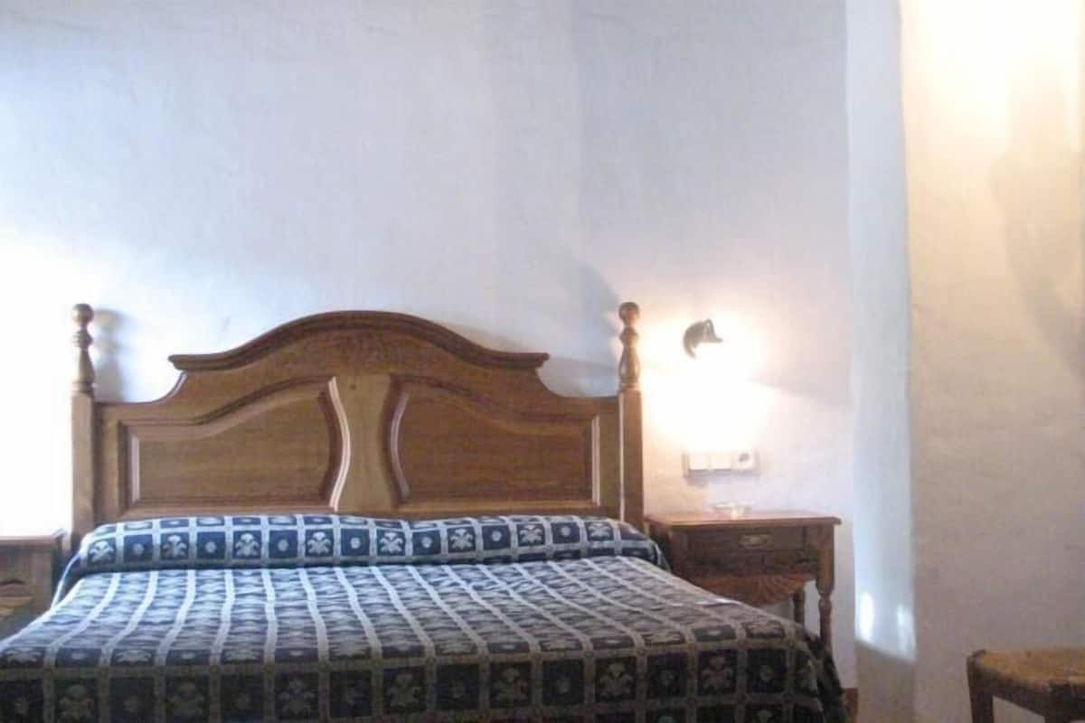 A bedroom with a wooden bed, patterned bedspread, bedside lamp, and a wardrobe.