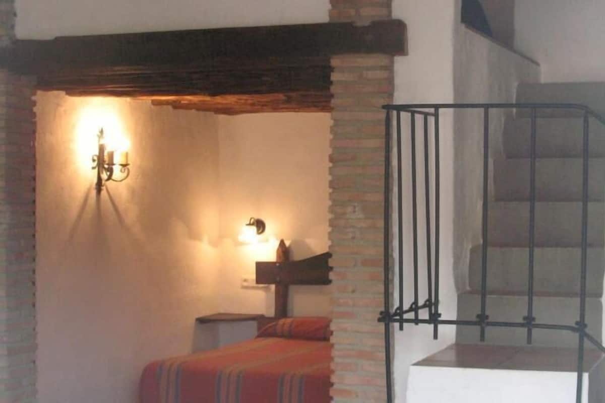 A room with a staircase, a bed with a striped blanket, and a wall-mounted light fixture.