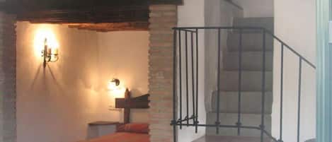 A room with a staircase, a bed with a striped blanket, and a wall-mounted light fixture.
