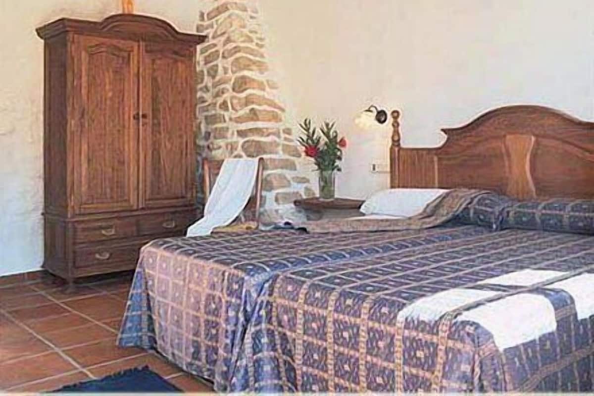 A bedroom with a wooden bed, a stone wall, and a wooden cabinet.
