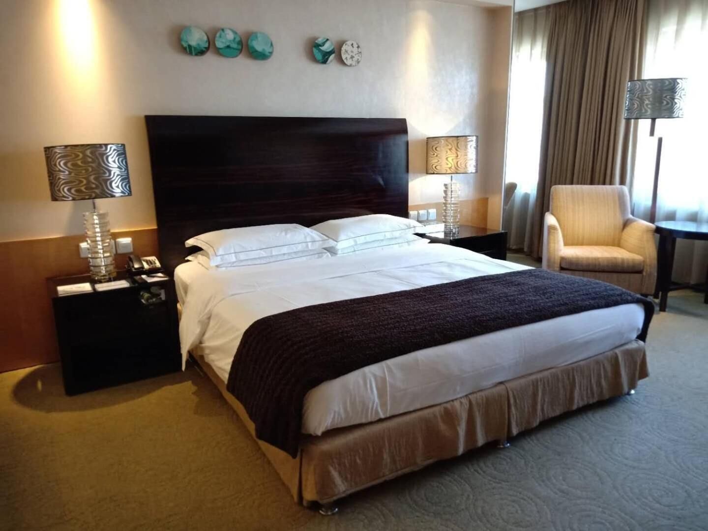 A hotel room with a large bed, two bedside tables with lamps, a chair, and decorative wall art.