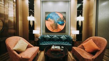 Um hall com sofá de couro, duas poltronas, uma mesa de centro e uma grande pintura abstrata.