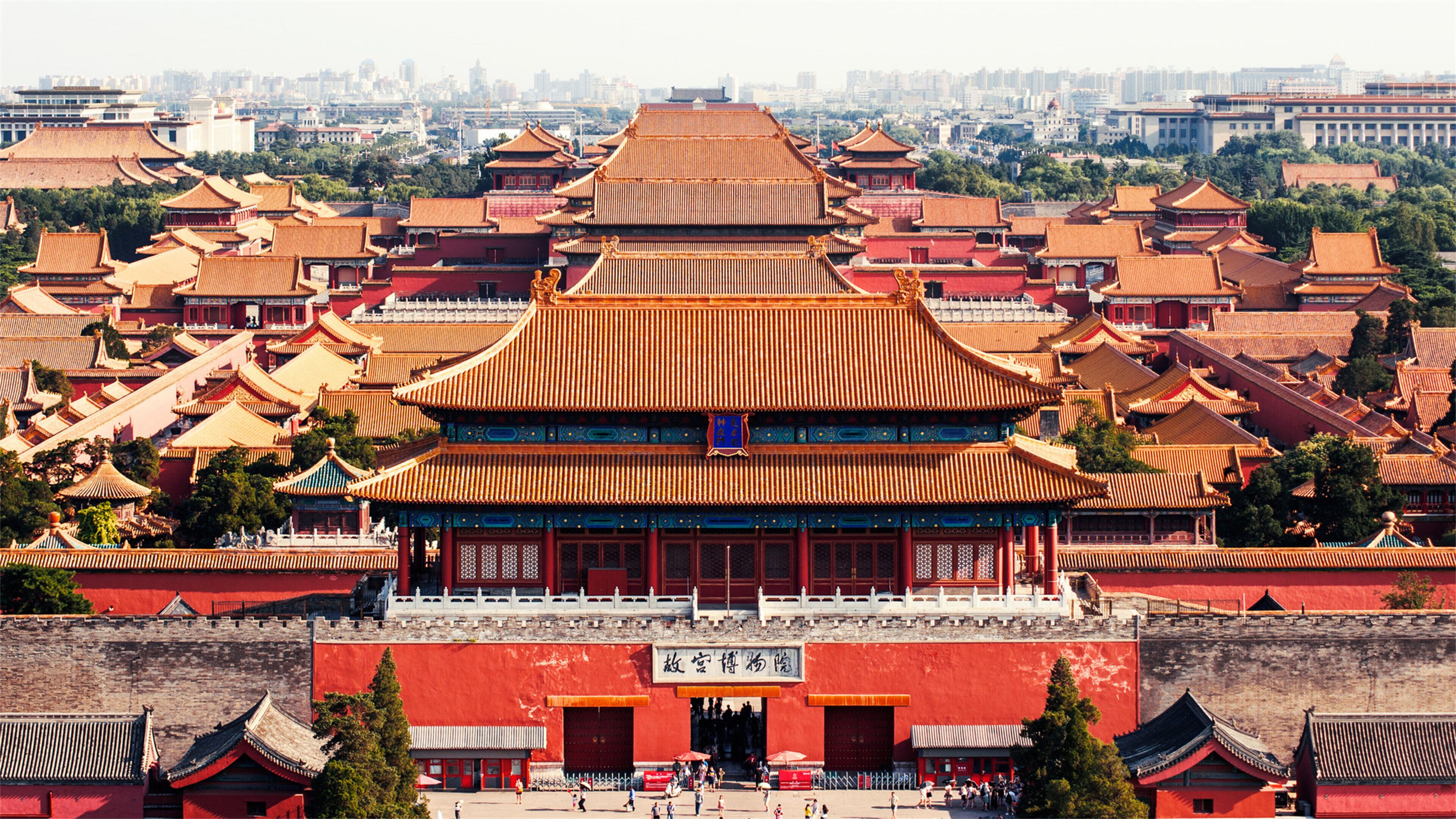 A traditional Chinese building with multiple tiers of roofs, a large open courtyard, and a red wall with a gate.