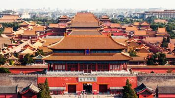 A traditional Chinese building with multiple tiers of roofs, a large open courtyard, and a red wall with a gate.