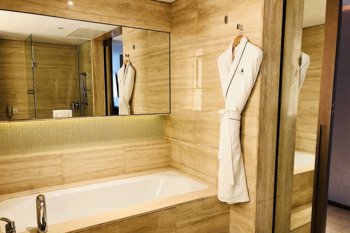 A modern bathroom with a large mirror, a bathtub, and two white bathrobes hanging on the wall.