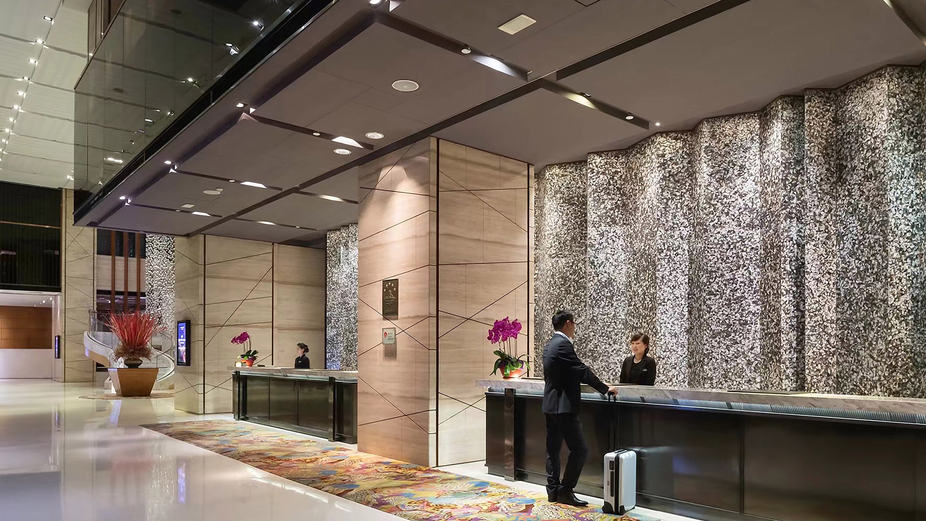 Un moderno vestíbulo de hotel con mostrador de recepción, una pared con diseño llamativo y una alfombra decorativa.