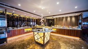 A modern hotel lobby with a central island featuring a decorative sculpture, a buffet with various food items, and a seating area with a television. - Marco Polo Parkside Beijing (Beijing)