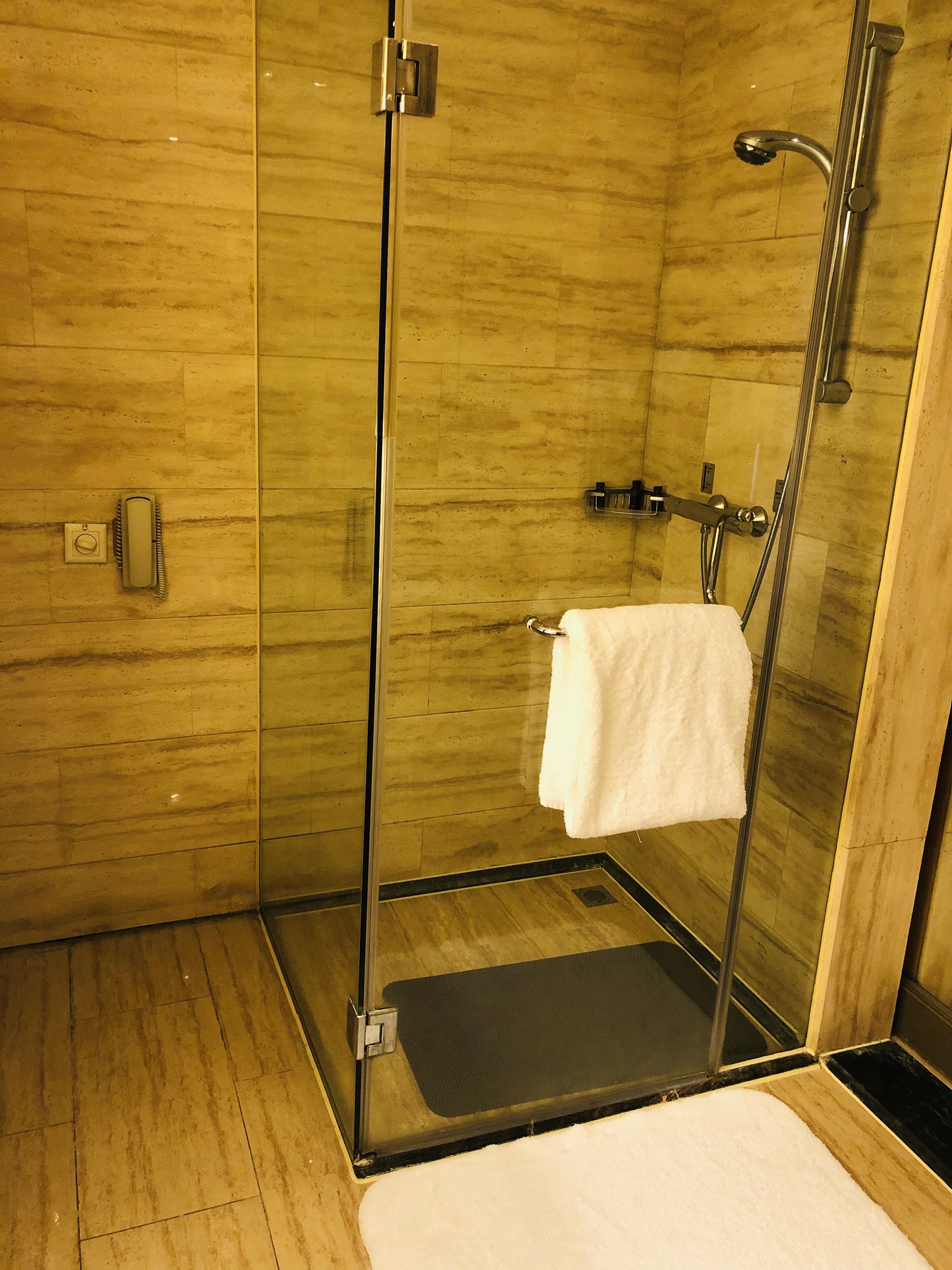 Una doccia moderna con porta in vetro, un asciugamano bianco appeso al muro e un pavimento in legno.