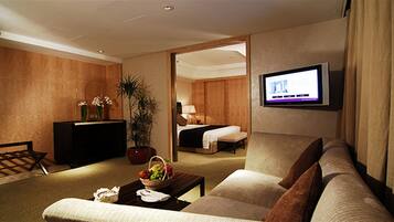 Ein Hotelzimmer mit einer Sitzecke, einem Fernseher, einem Schreibtisch mit Computer sowie einem Bett und einer Zimmerpflanze.