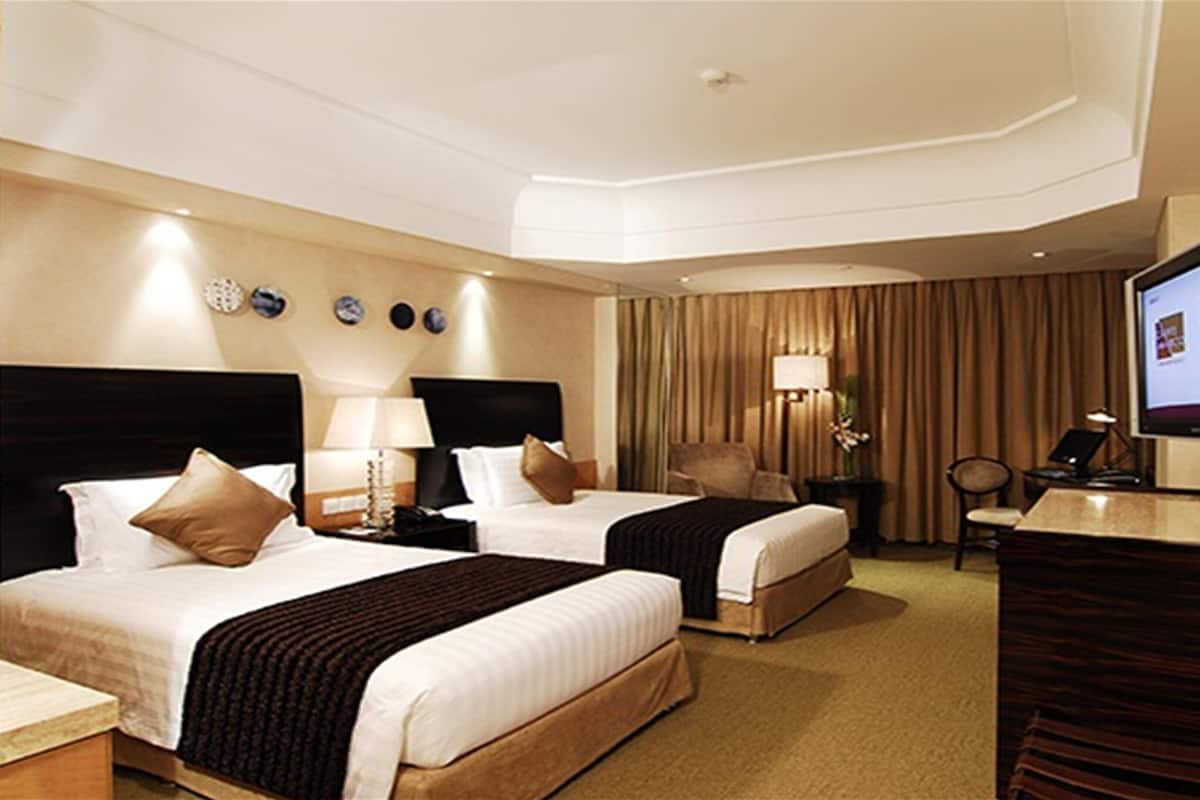 A hotel room with two beds, a desk, a chair, a television, and a lamp.