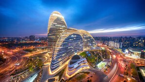 A modern, uniquely shaped hotel with multiple curved levels and a prominent dome structure, surrounded by a well-lit urban area with roads and other buildings. - Marco Polo Parkside Beijing (Beijing)