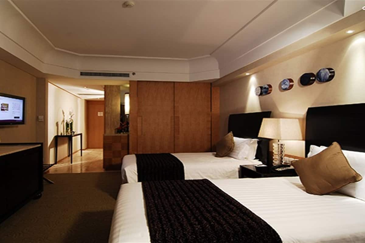 A hotel room with two beds, a TV, a desk, and a bathroom visible through an open door.