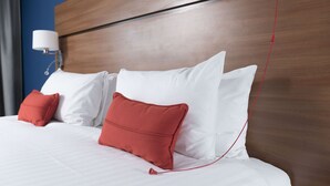 A neatly made bed with white and red pillows, a wooden headboard, and a wall-mounted lamp. - Holiday Inn Express Birmingham Star City by IHG (Birmingham)