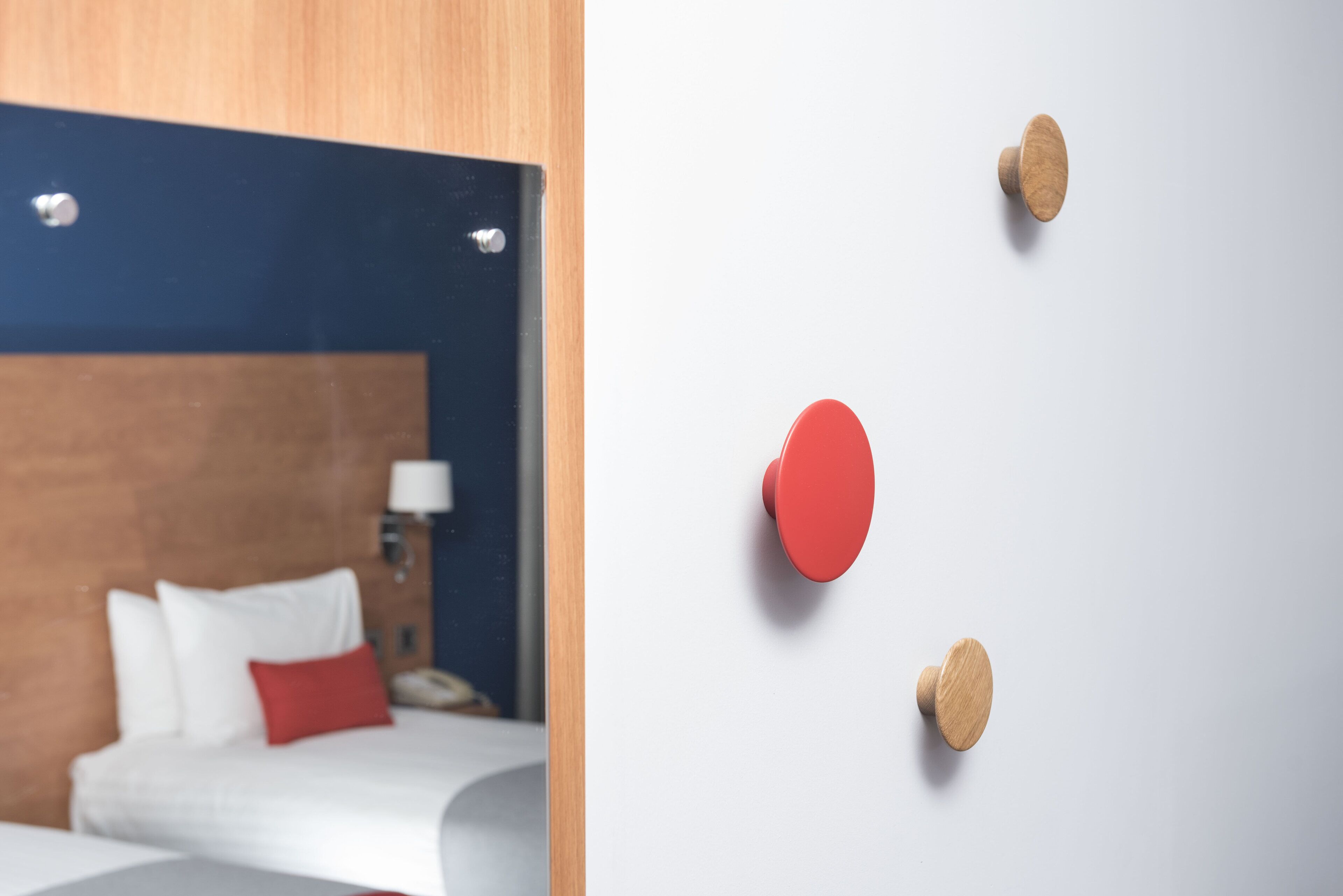 A hotel room with a wooden headboard, a bed with white and red bedding, and a nightstand with a lamp.