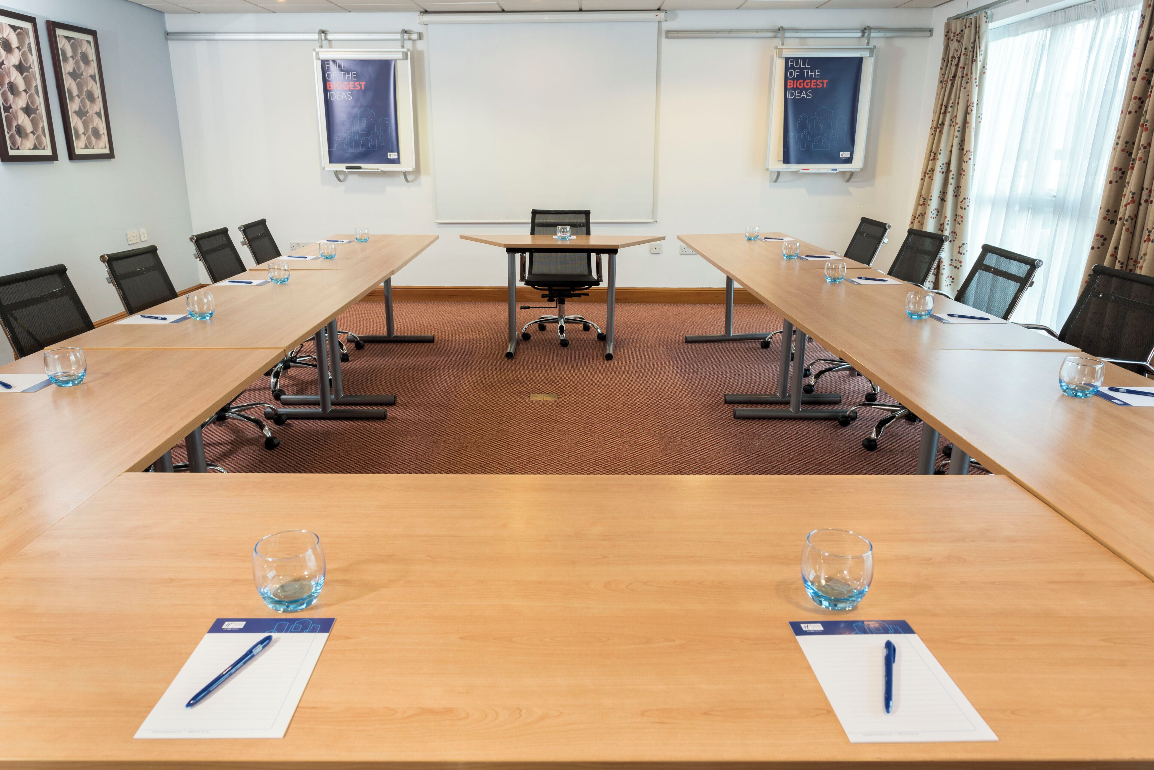 A conference room with a long table, chairs, and two posters on the walls.