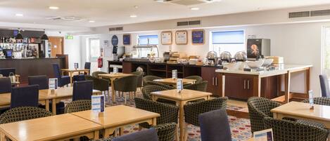 A hotel lobby with multiple seating areas, a bar, and a kitchen in the background.