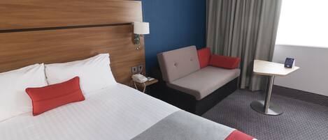 Una habitación de hotel con dos camas, un sofá, una mesita, una lámpara y un teléfono.