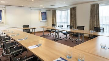 A conference room with long tables, chairs, and a projector screen.