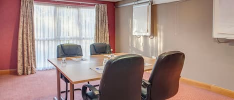 A conference room with a table, chairs, a projector screen, and curtains.