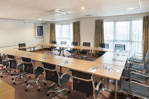 A conference room with long tables, chairs, and a projector screen.
