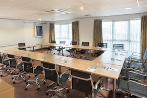 Une salle de conférence équipée de longues tables, de chaises et d’un écran de projection.