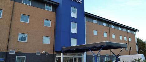 Un hotel Holiday Inn Express con una fachada destacada en azul y marrón, amplias ventanas y una zona de entrada cubierta.