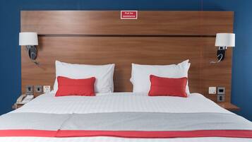 A hotel room with a wooden headboard, two bedside lamps, a telephone, and a red and white bedspread.