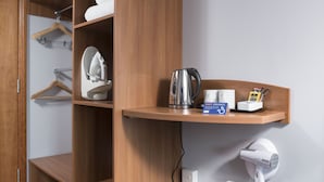 A hotel room with a wooden wardrobe, a shelf with a kettle, a hairdryer, and a box of hot drinks. - Holiday Inn Express Birmingham Star City by IHG (Birmingham)