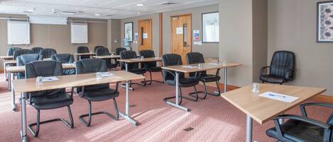 A conference room with multiple tables and chairs, equipped with water bottles and papers.