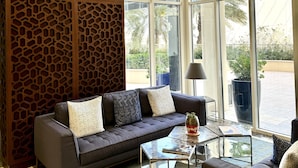 A modern living room with a dark grey sofa, a glass coffee table, and a wooden decorative panel. - Mysk Al Fateh Bahrain (Manama)