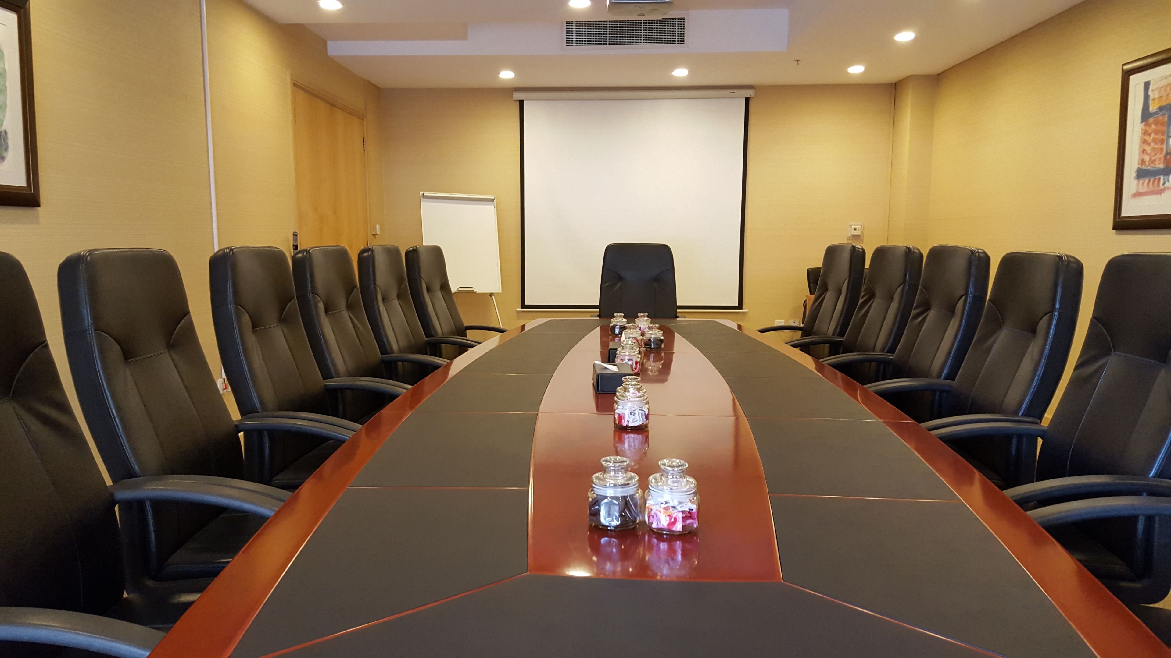 A conference room with a long table, black leather chairs, and a projector screen.