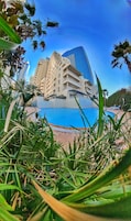 Un hotel con piscina, palmeras y edificios modernos al fondo.